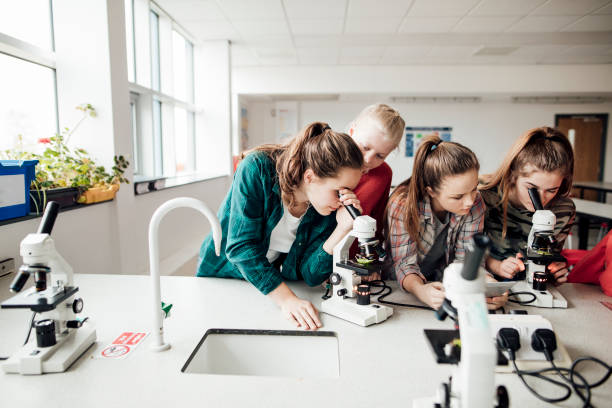 Group of teenage girls looking down microscope at school while learning STEM.